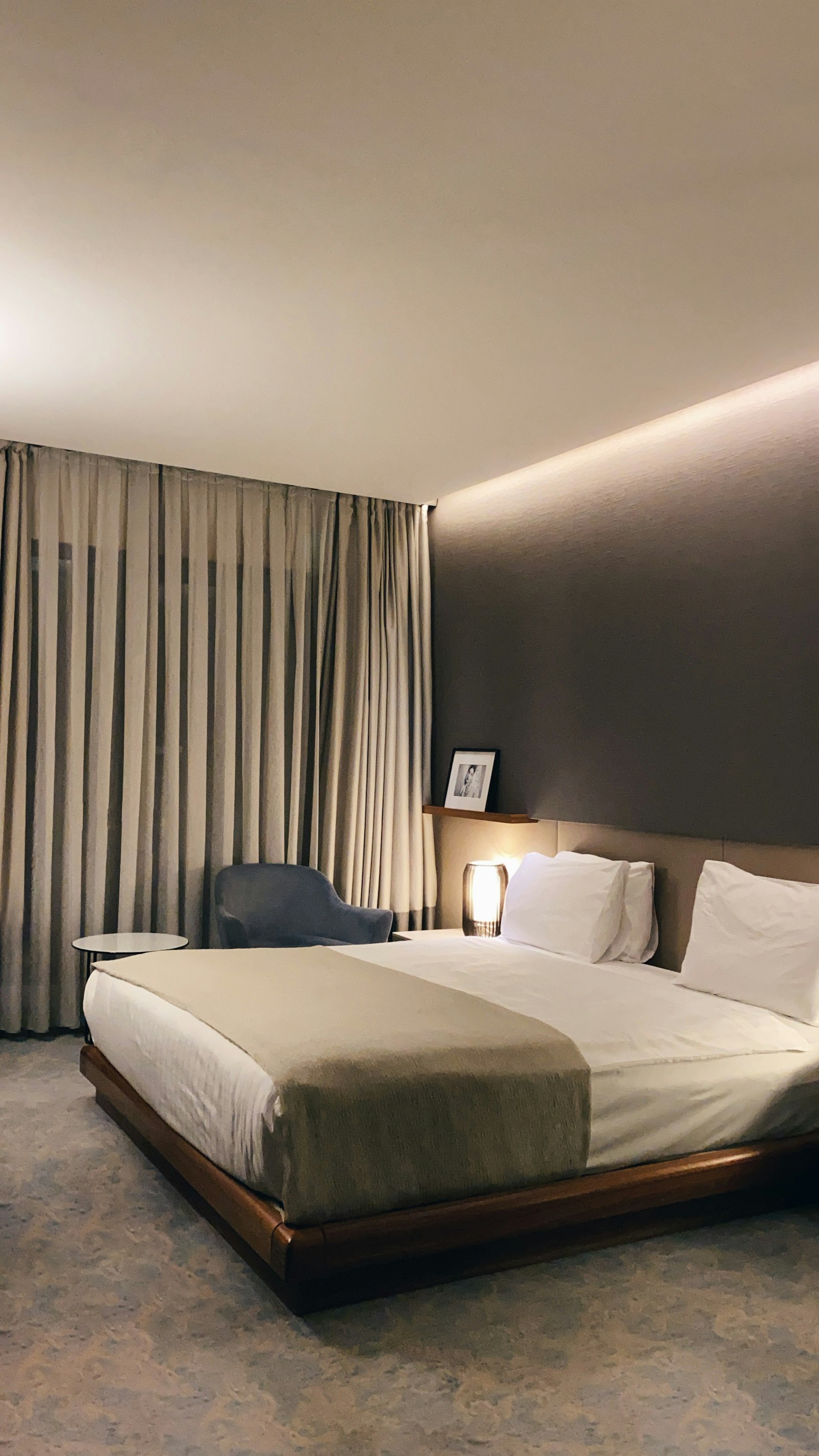 Zimmer 4: Bett mit Holzrahmen, Sessel und Leselampe, Vorhang bis zum Boden.